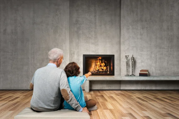 Opa mit Kind auf einem Kissen in Zimmer mit Holzboden und Kamin in einer Betonwand