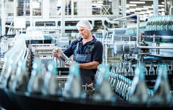 Mann mit Haarnetz der Gerolsteiner Flasche in der Hand hält in einer Flaschenfabrik