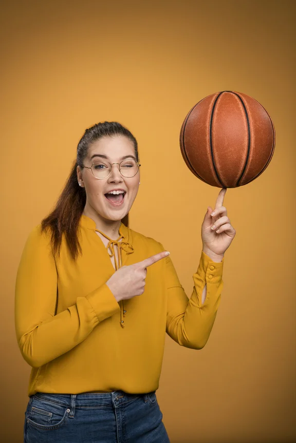 Weibliche Person mit gelbem Pullover vor gelber Wand balanciert Basketball auf einem Finger