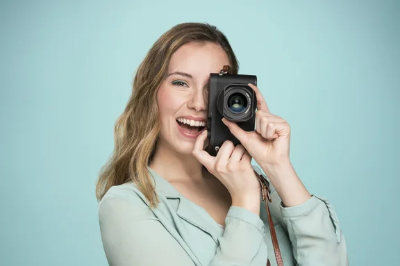 Weibliche Person mit Kamera vor hellblauem Hintergrund