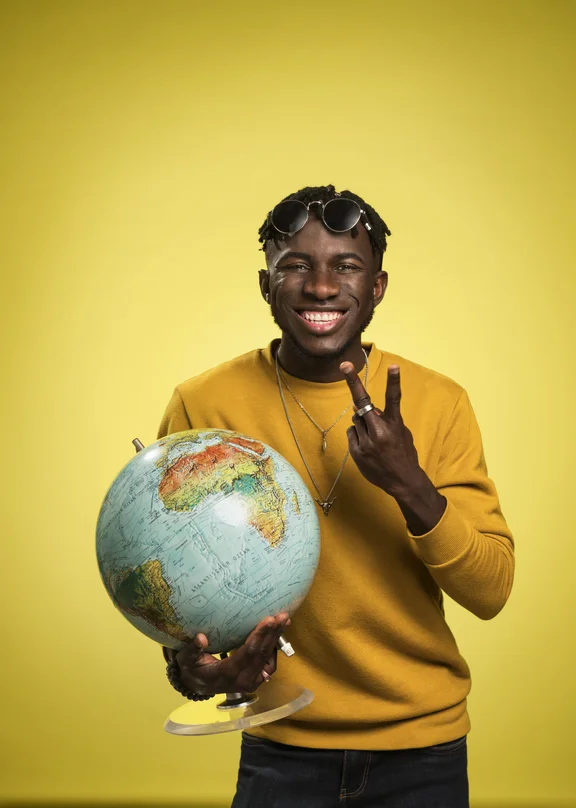 Junge männliche Person mit gelbem Pullover vor gelbem Hintergrund mit Globus in der Hand