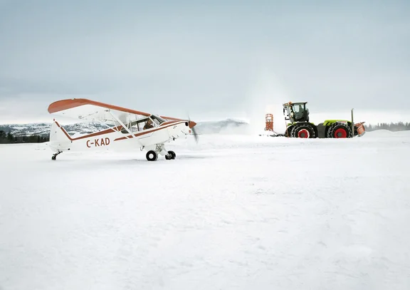 Propellerflugzeug und Trecker stehen auf mit Schnee bedecktem Berg, Trecker schiebt Schnee zur Seite