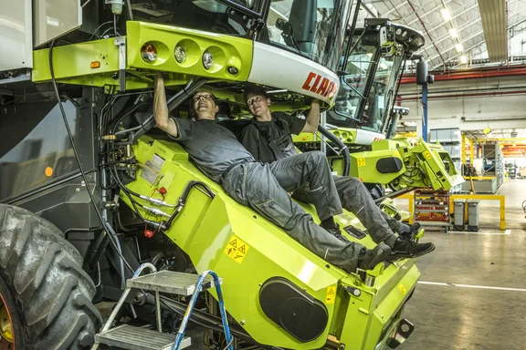 Zwei Männer, die vorne auf einem Mähdrescher liegen und von unten am Führerhaus arbeiten