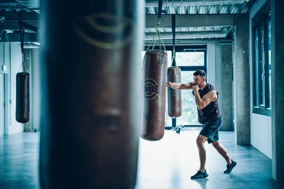 Männliche Person, die gegen einen Boxsack schlägt in einem bläulichen Raum voller Boxsäcke