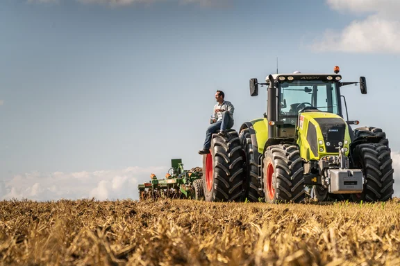 Mann sitzt auf dem Rad eines großen Treckers auf einem Kornfeld