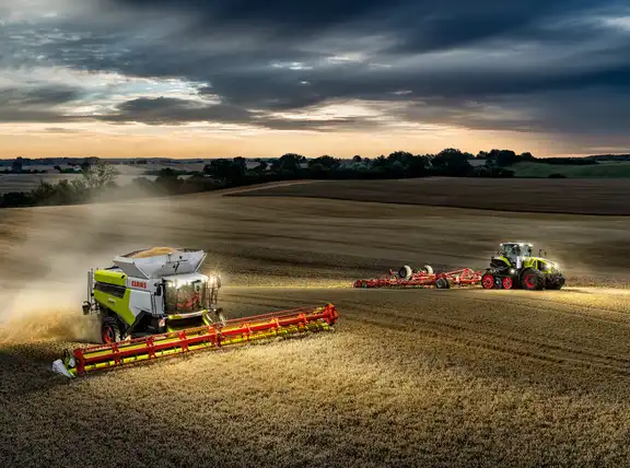 Ein Mähdrescher und ein Trecker mit Grubber auf einem Kornfeld am Abend