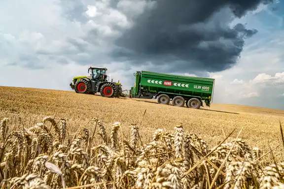 Trecker, der einen großen grünen Anhänger über ein gemähtes Kornfeld bergauf zieht