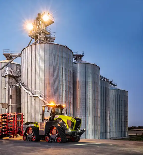 Landmaschine "Raupe" steht neben drei großen Silos