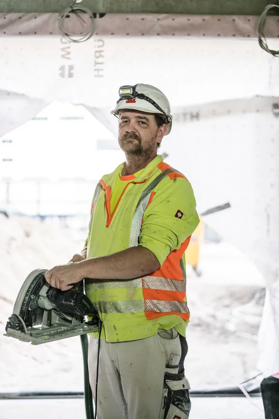 Arbeiter in Warnweste mit Helm, der eine Kreissäge trägt