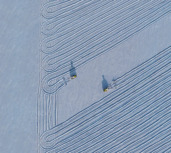 Zzwei Trecker fahren über verschneites Land, von oben