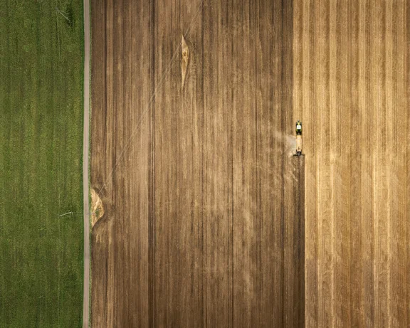 Halb gegrubbertes Kornfeld von Oben mit Trecker, grünes Feld links