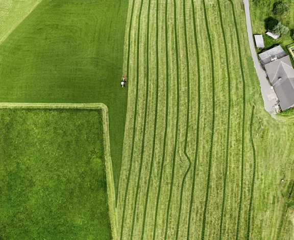 Halb geschnittenes Grasfeld mit Trecker von oben