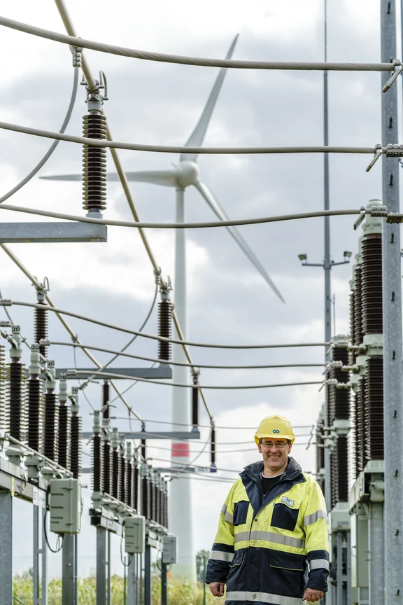 Mann in Warnjacke und Helm steht in einem Umspannwerk