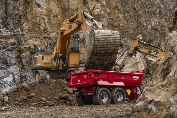 Bagger steht auf Erdhaufen an einem Sandberg und belädt kleinen Anhänger mit Erde