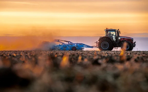 Trecker, der einen Grubber bei Sonnenaufgang über ein Feld zieht, Blick von der Seite