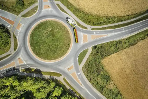 Kreisverkehr mit fünf ausfahrten umgeben von Feldern, Mähdrescher auf der Straße