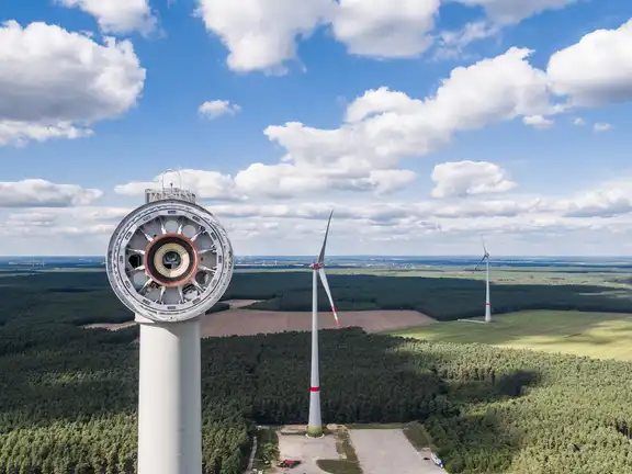 Windrad im Bau oben von der Seite, Windräder und Wald im Hintergrund