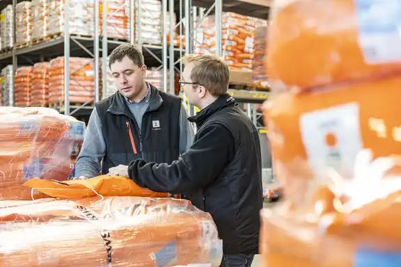 Zwei redende Männer in der Mitte, umgeben von Papiersäcken auf Paletten