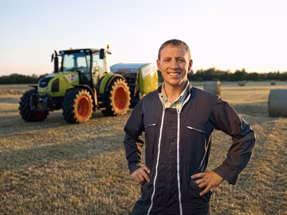 Mann in Arbeitsanzug auf einem Feld vor einem großen Trecker