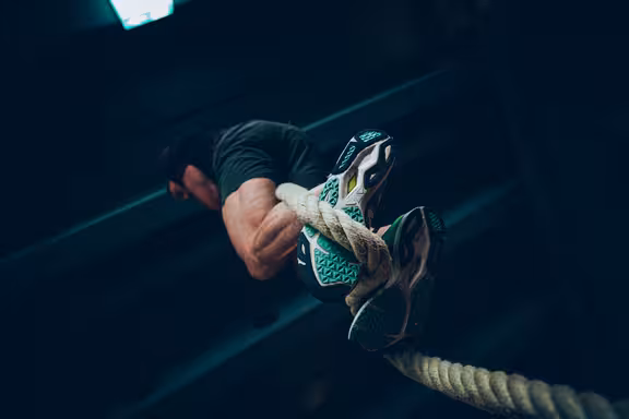 Männliche Person, die an einem Seil hochklettert, Blick von unten auf die Turnschuhe am Seil