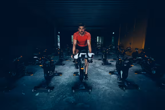 Männliche Person in Sportkleidung auf einem Fahrrad in einem Raum voller Fahrräder, sehr dunkel