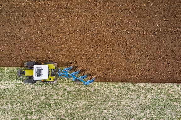 Trecker grubbert eine Wiese, von oben