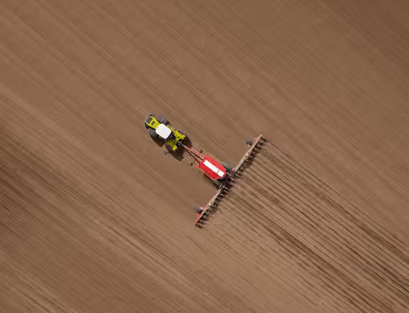 Trecker fährt über ein braunes Feld, von oben