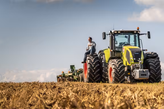 Mann sitzt auf dem Rad eines großen Treckers auf einem Kornfeld