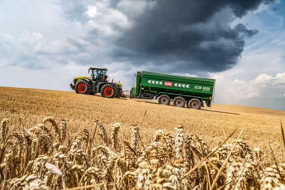 Trecker, der einen großen grünen Anhänger über ein gemähtes Kornfeld bergauf zieht