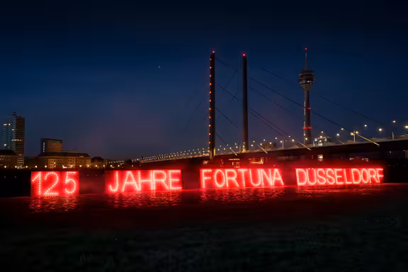 rot leuchtende Schrift: "125 Jarhe Fortuna Düsseldrf" vor der Rheinbrücke bei Nacht