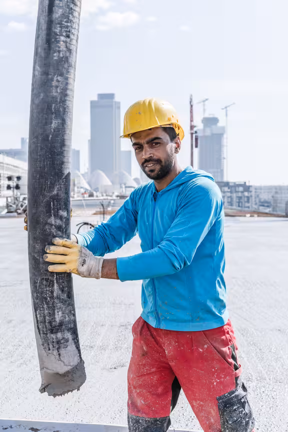 Arbeiter mit Helm, der einen Betonschlauch hält