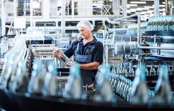 Mann mit Haarnetz der Gerolsteiner Flasche in der Hand hält in einer Flaschenfabrik