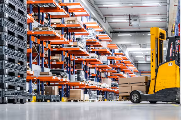 Lagerhalle mit Regalen und gelben Stapler mit Kartons