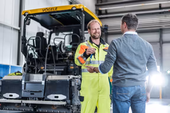 Mann in Warnanzug übergibt Schlüssel einem anderen Mann