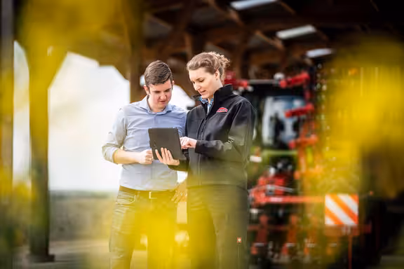 Frau und Mann in Arbeitskleidung mit Tablet in der Hand vor einem Trecker