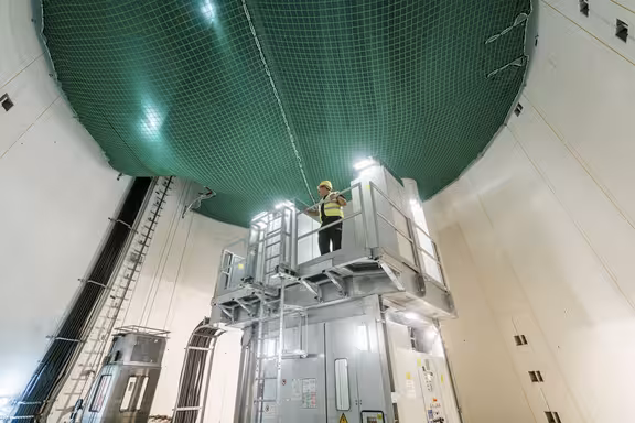 Mann auf einem Aufbau in einem runden Raum, ein grünes Netzt grenzt den Raum von oben ab