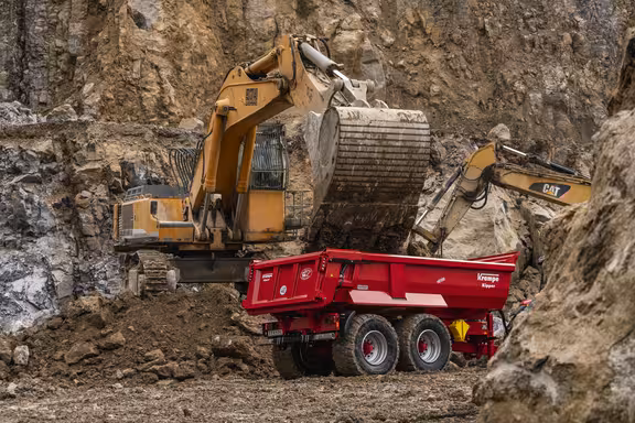 Bagger steht auf Erdhaufen an einem Sandberg und belädt kleinen Anhänger mit Erde