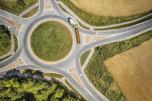 Kreisverkehr mit fünf ausfahrten umgeben von Feldern, Mähdrescher auf der Straße