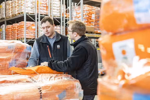 Zwei redende Männer in der Mitte, umgeben von Papiersäcken auf Paletten