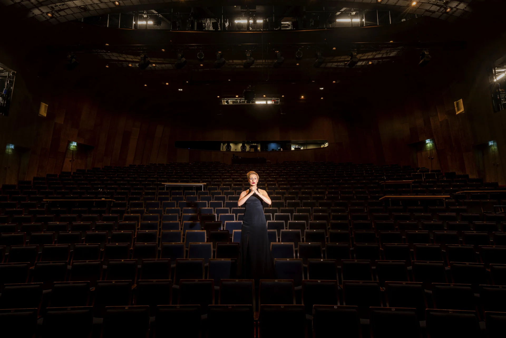 Lichtspot auf Peron im Kleid in der Mitte der Bühne eines leeren Theaters, Blick auf die Zuschauerstühle