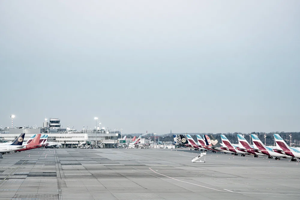 leeres Flughafenrollfeld, Flugzeuge links und rechts, Gebäude im Hintergrund