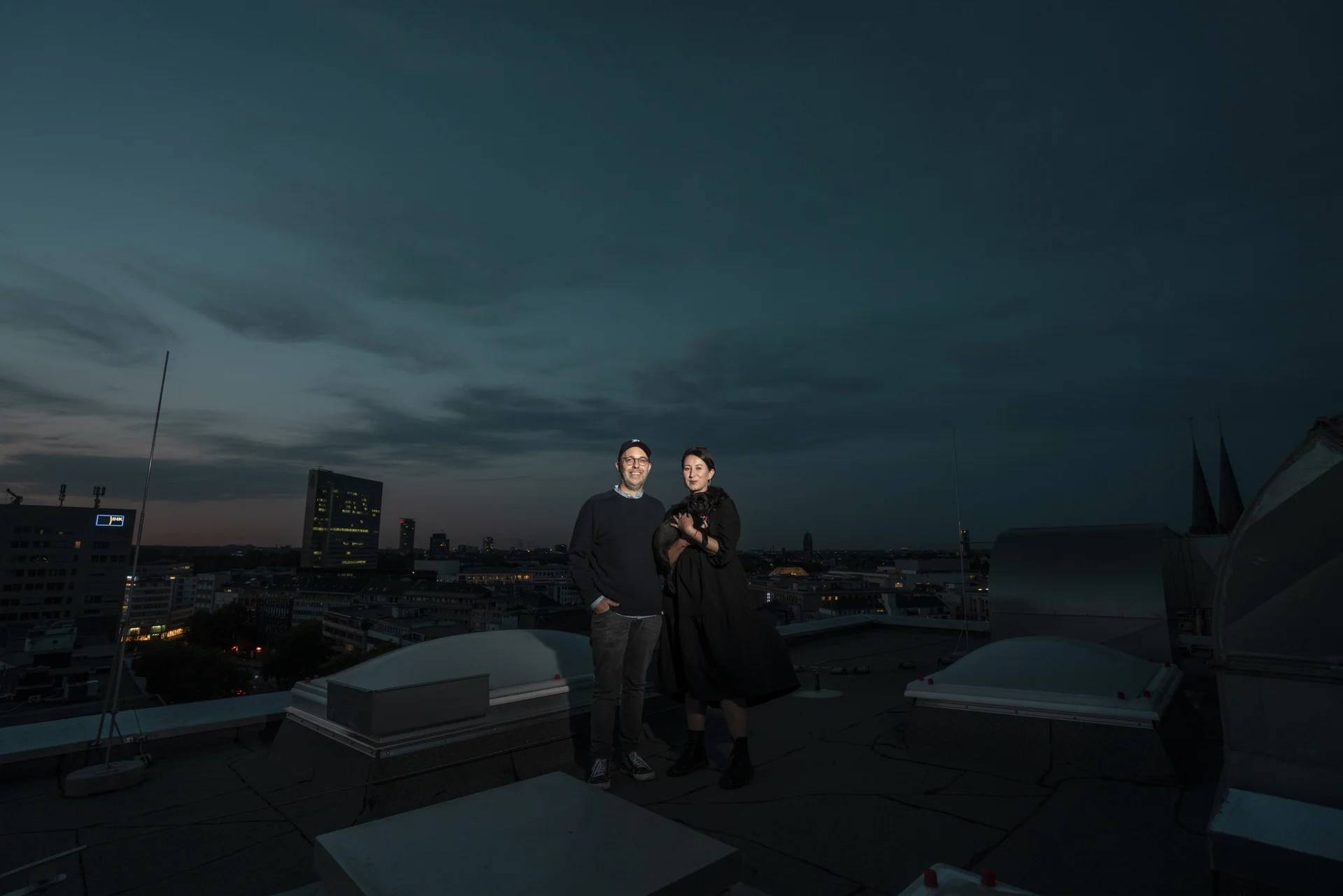Lichtspot auf zwei Personen die auf einem Dach in einer großen Stadt stehen, die Dächer der Stadt im Hintergrund