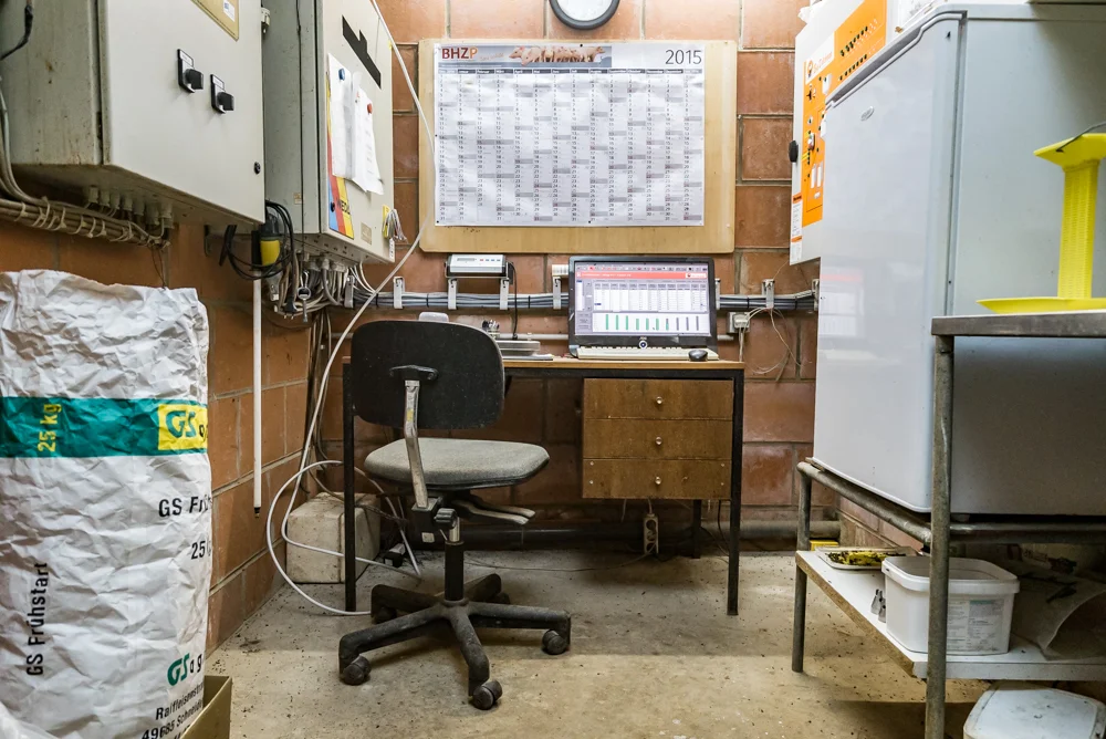 Schreibtisch mit drei Schubladen, Bürostuhl in einem kleinen Raum mit technischen Schränken