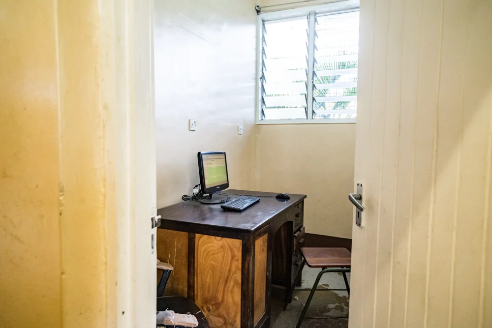 Holzschreibtisch mit Computer und einfachem Stuhl in einem kleinen Raum mit Fenster